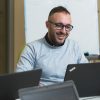 Uomo con occhiali che lavora ad un computer portatile e sorride.
