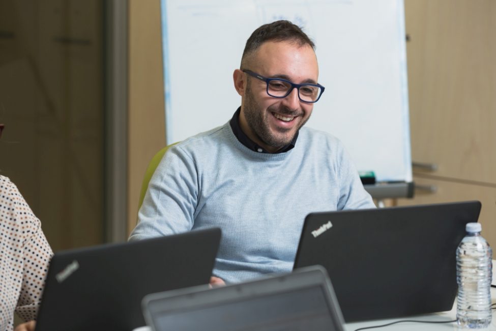 Uomo con occhiali che lavora ad un computer portatile e sorride.