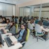 Gruppo di persone sedute alle proprie postazioni che indossano delle cuffie e lavorano al computer.