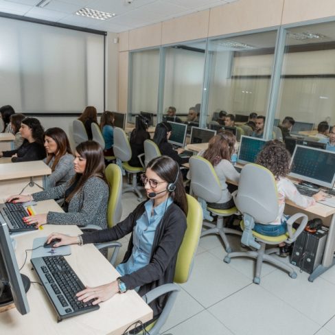 Gruppo di persone sedute alle proprie postazioni che indossano delle cuffie e lavorano al computer.