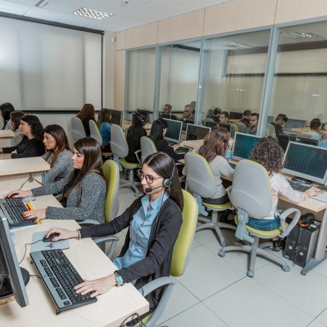 Galleria fotografica Gruppo di persone sedute alle proprie postazioni che indossano delle cuffie e lavorano al computer.