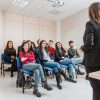 Donna in piedi che parla ad un gruppo di persone sedute.