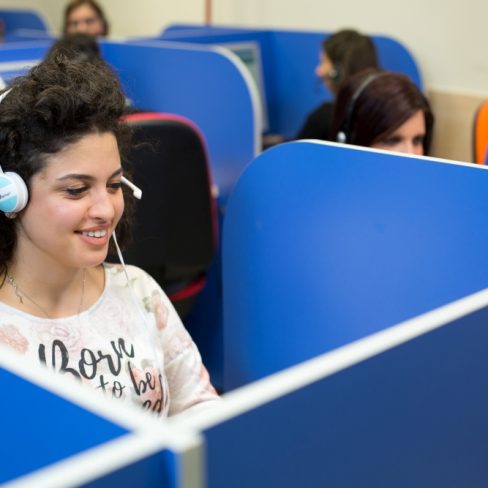 Operatrice che indossa delle cuffie e sorride mentre guarda il computer.