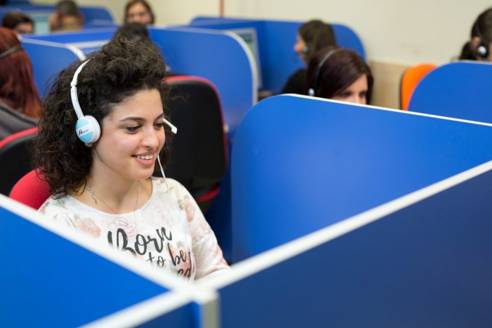 Operatrice che indossa delle cuffie e sorride mentre guarda il computer.