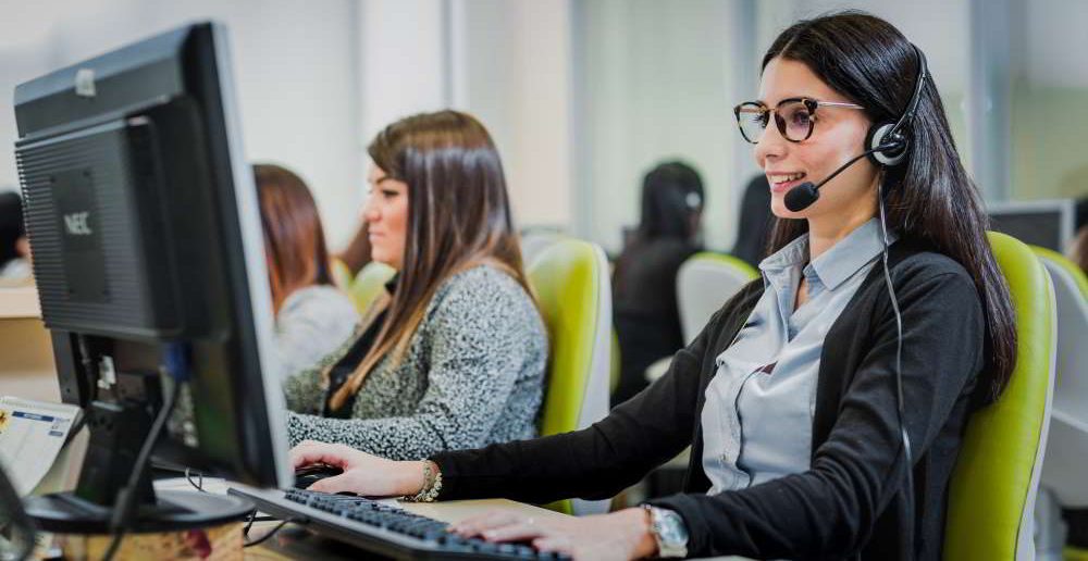 Operatrici sedute nella propria postazione che indossano delle cuffie e lavorano al computer.