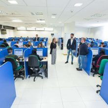 Grande stanza in cui vi sono tanti operatori ciascuno nelle proprie postazioni. Ogni operatore indossa delle cuffie e lavora al computer.