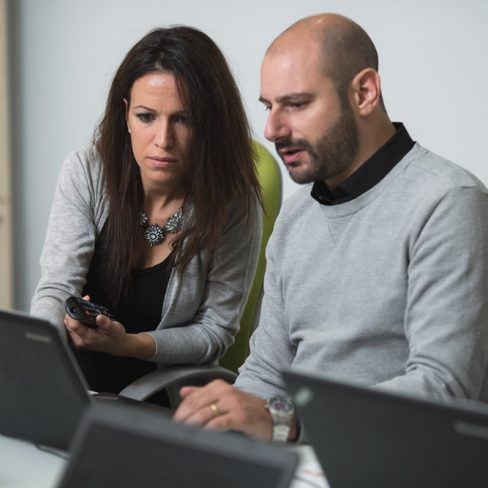 Uomo e donna seduti di fronte al computer che lavorano assieme.