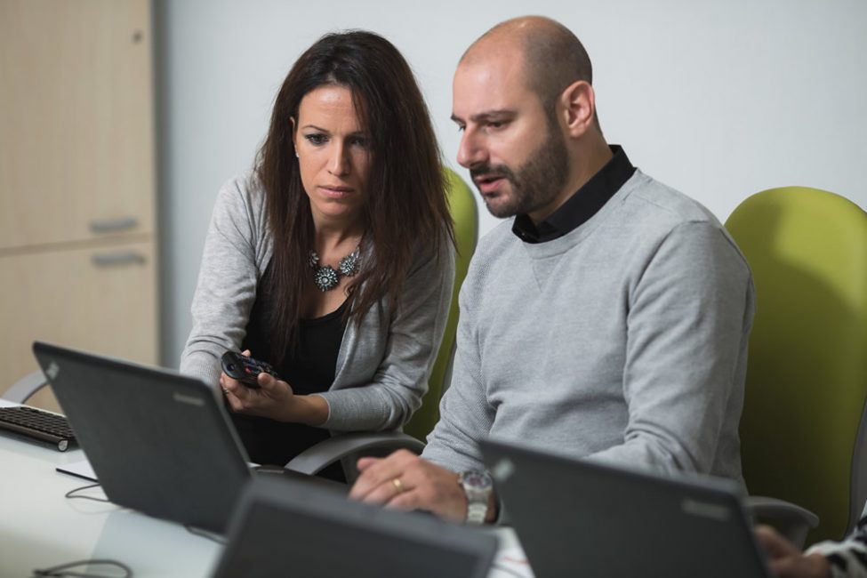 Uomo e donna seduti di fronte al computer che lavorano assieme.
