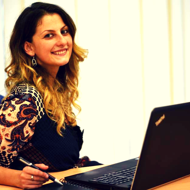 Caterina-Torrisi Donna davanti a un computer portatile che sorride e tiene in mano una penna.