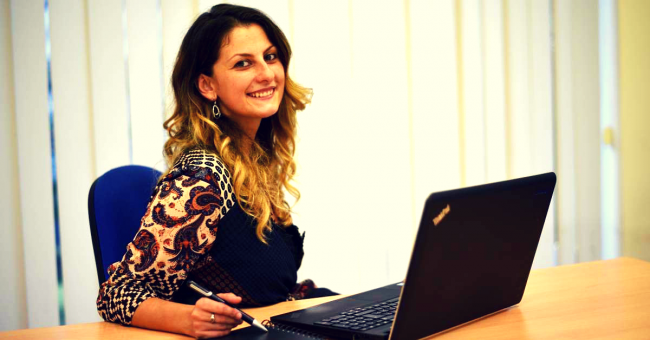 Donna davanti a un computer portatile che sorride e tiene in mano una penna.