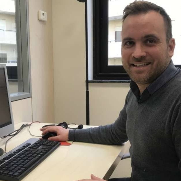 Antonino-Caridi Primo piano uomo che sorride seduto davanti al computer.