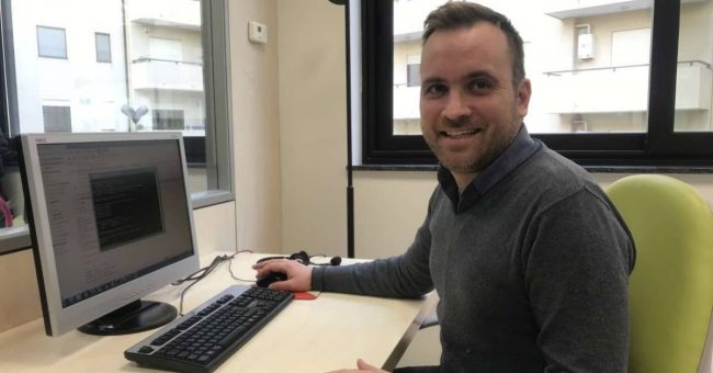 Antonino-Caridi Primo piano uomo che sorride seduto davanti al computer.