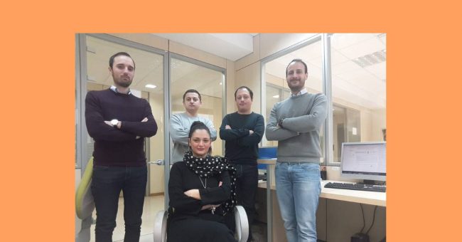 Gruppo di persone in piedi con le mani conserte e una persona seduta su una sedia.