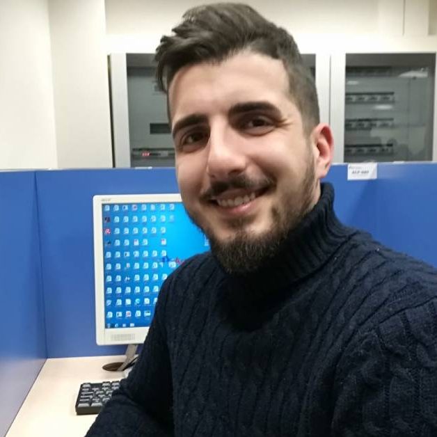 Angelo-Masullo Ragazzo in ufficio che sorride seduto su una sedia. Sullo sfondo una postazione con il computer.