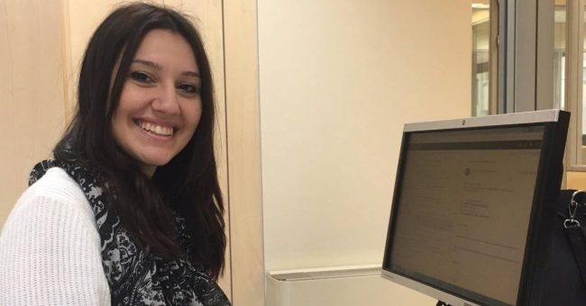 Ragazza con maglione e sciarpa davanti al computer che sorride