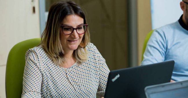 Donna con occhiali seduta su una sedia verde che lavora al computer