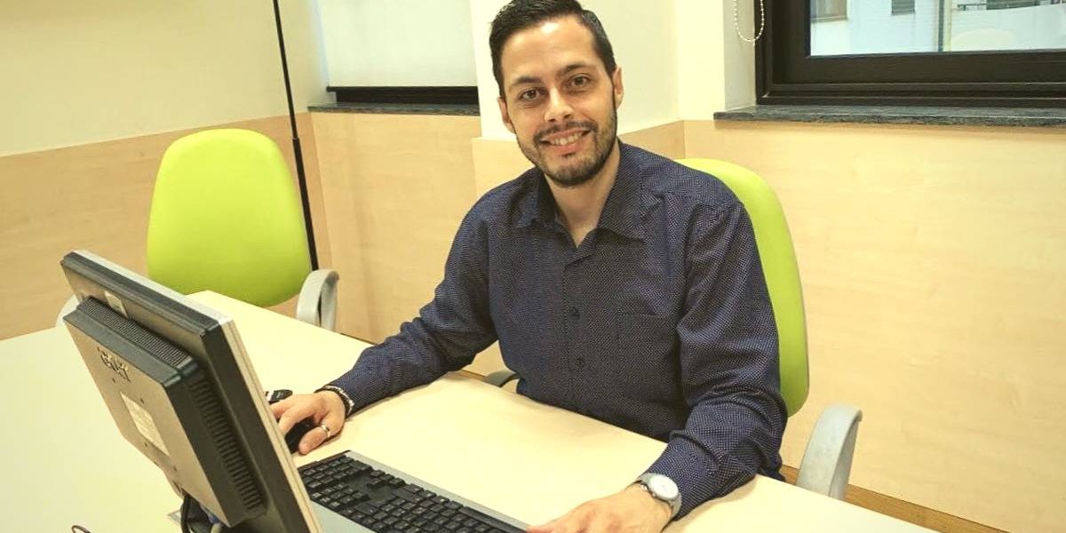 Roberto-Pugliatti Uomo che sta sorridendo in ufficio ed è seduto su una sedia verde di fronte al computer