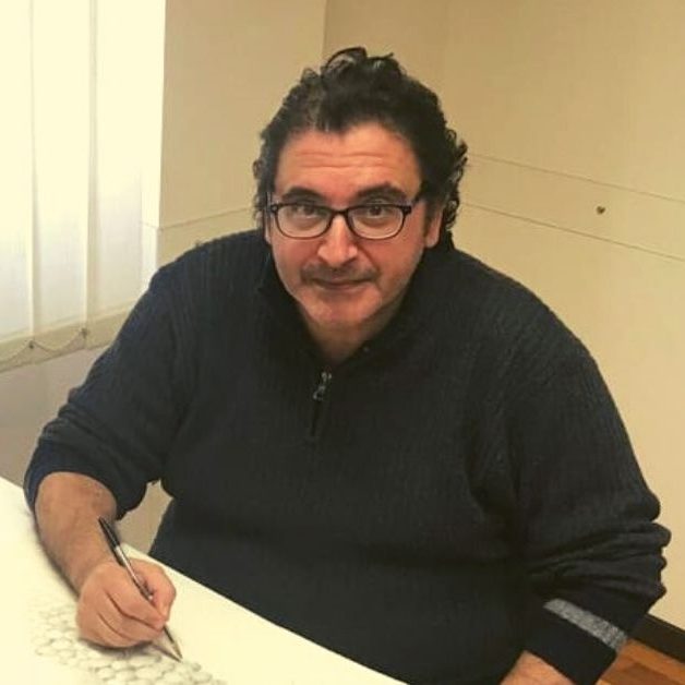 Emiliano-Falzone Uomo con occhiali seduto alla scrivania che disegna con una penna nera