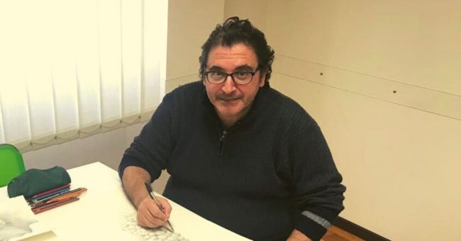 Uomo con occhiali seduto alla scrivania che disegna con una penna nera
