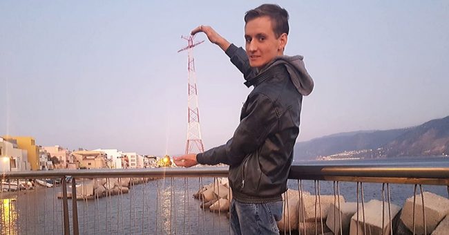 Ragazzo in piedi appoggiato al corrimano di un ponticello sul mare