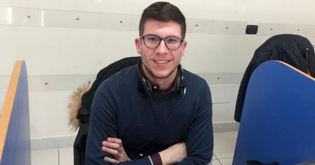 Ragazzo con occhiali seduto alla scrivania con le braccia conserte