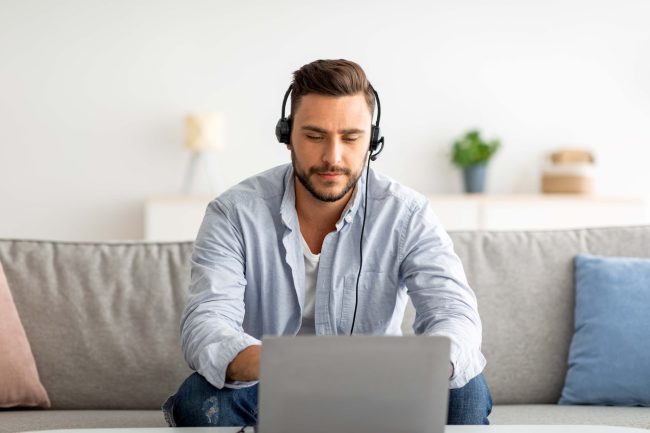 Ragazzo seduto sul divano che indossa delle cuffie e lavora al computer.