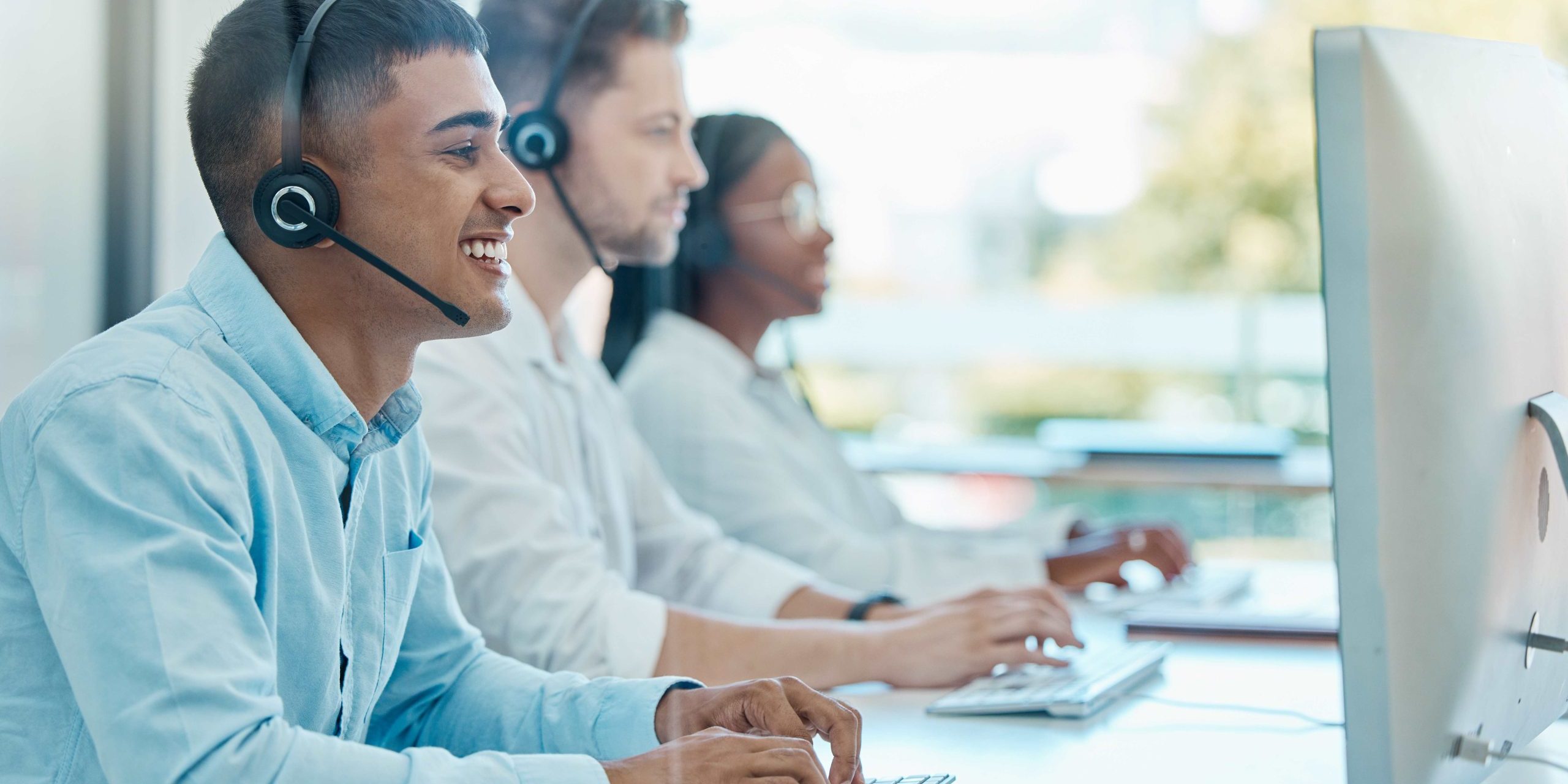 CRM cos’è e a cosa serve Gruppo di persone che indossano delle cuffie e ridono mentre lavorano al computer.