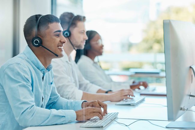Gruppo di persone che indossano delle cuffie e ridono mentre lavorano al computer.