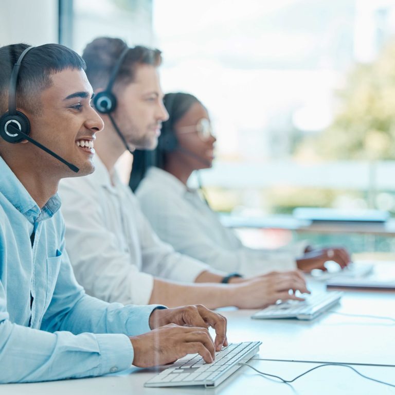 CRM cos’è e a cosa serve Gruppo di persone che indossano delle cuffie e ridono mentre lavorano al computer.